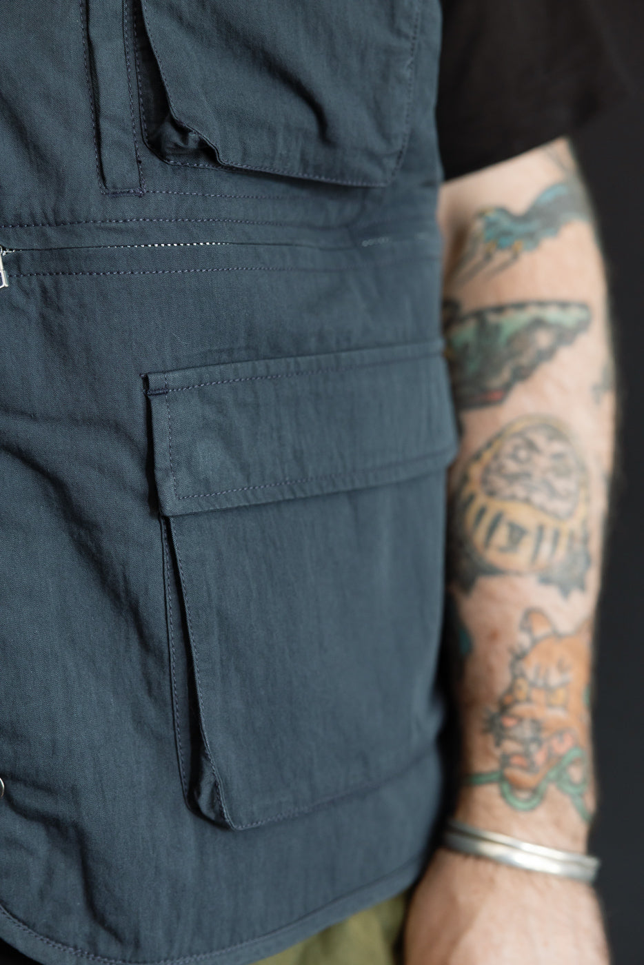 Close-up side view of a dark grey utility vest showing large cargo pocket and fabric texture.