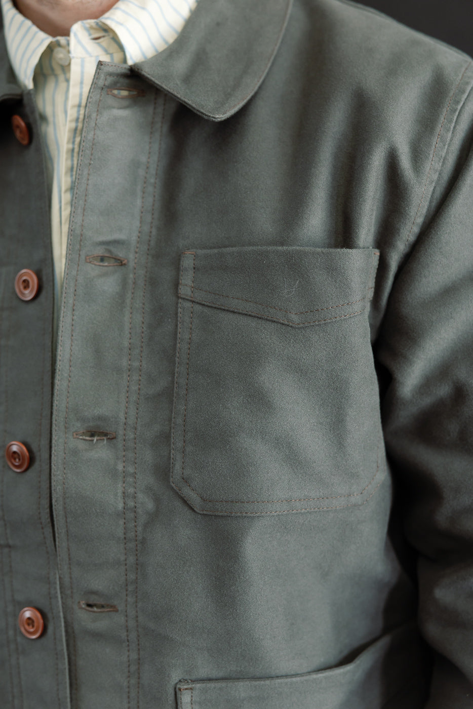 Close-up, left side view of a grey canvas chore jacket showing the chest pocket and fabric texture.