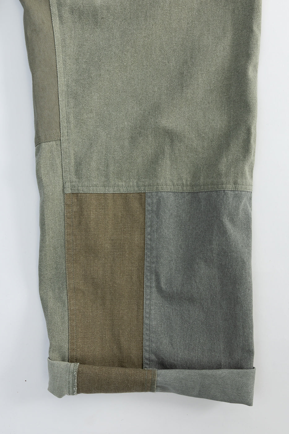 Close-up of front pant leg, showing olive patchwork fabric and cuffed hem detail.