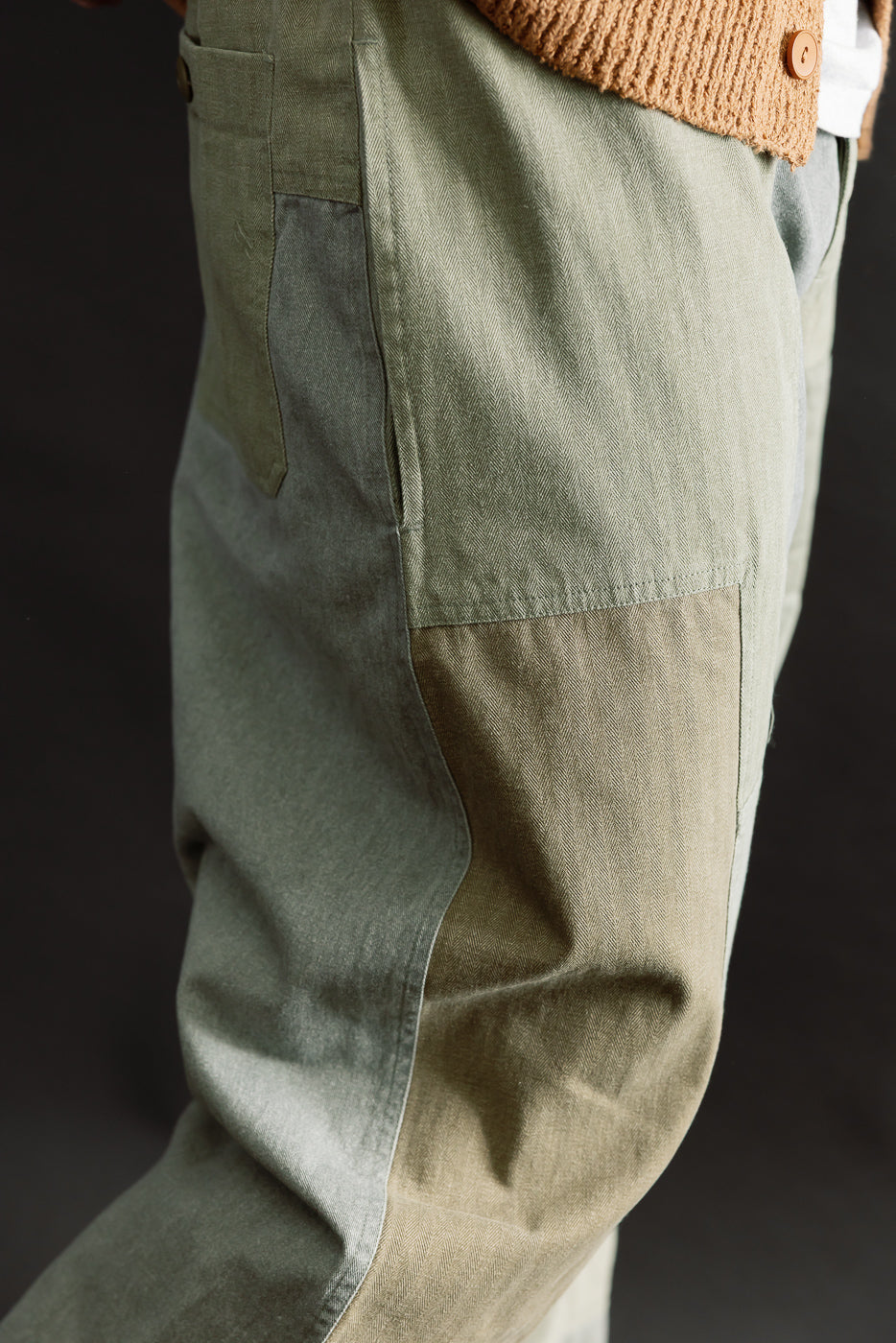 Close-up of male model's left side wearing olive patchwork pants, showing pocket and textured fabric, model is 5'9