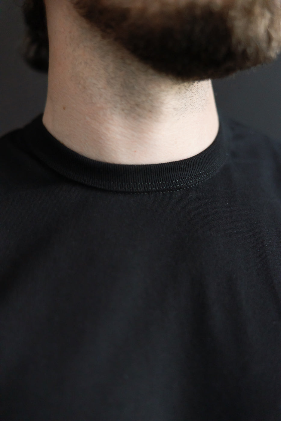 Close-up of heavyweight black t-shirt crew neckline, front detail on male model, athletic build