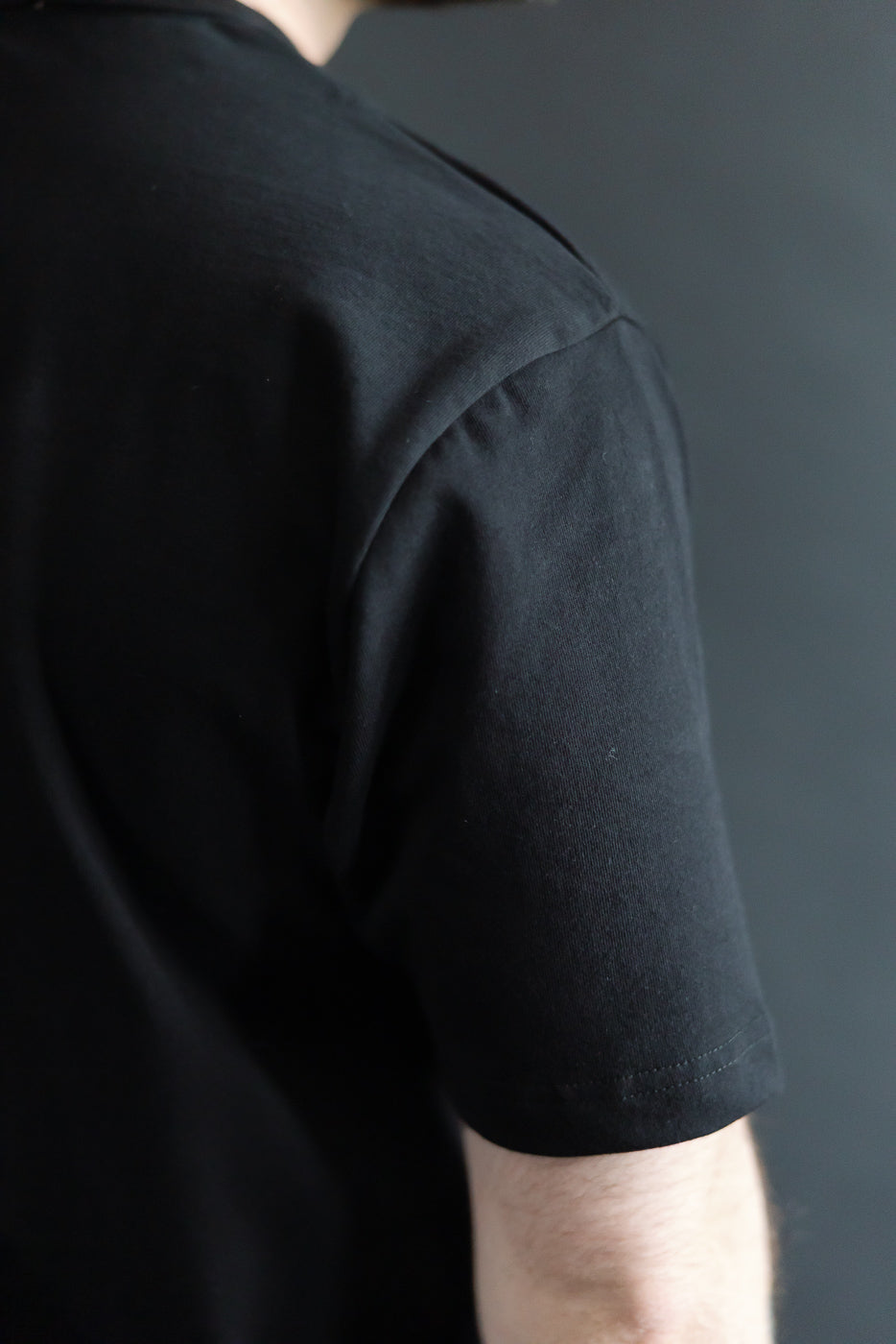 Close-up of male model's back right side wearing heavyweight black boxy t-shirt, sleeve and shoulder detail, 5'9