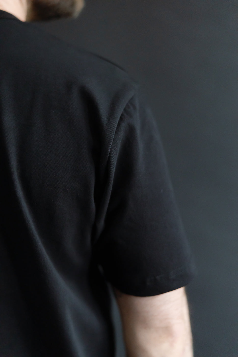 Close-up of male model’s back right shoulder in black heavyweight boxy T-shirt, sleeve seam detail visible