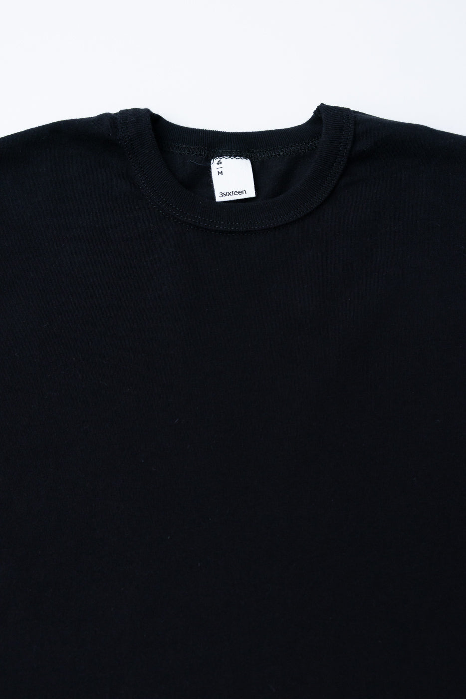 Close-up of black heavyweight boxy t-shirt front showing crew neck, collar seam, and neck tag.