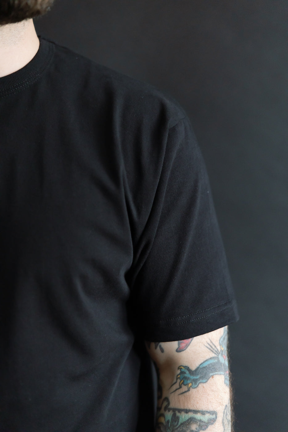 Close-up of front left shoulder and sleeve of heavyweight black boxy t-shirt on male model, 5'9