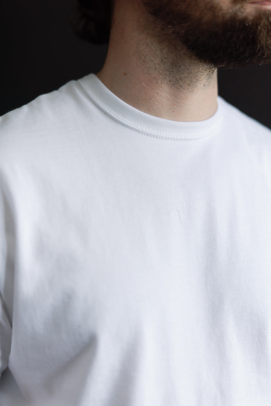 Close-up front of heavyweight white boxy t-shirt, male model 5'9 165lbs athletic build, fabric texture and crew neckline detail