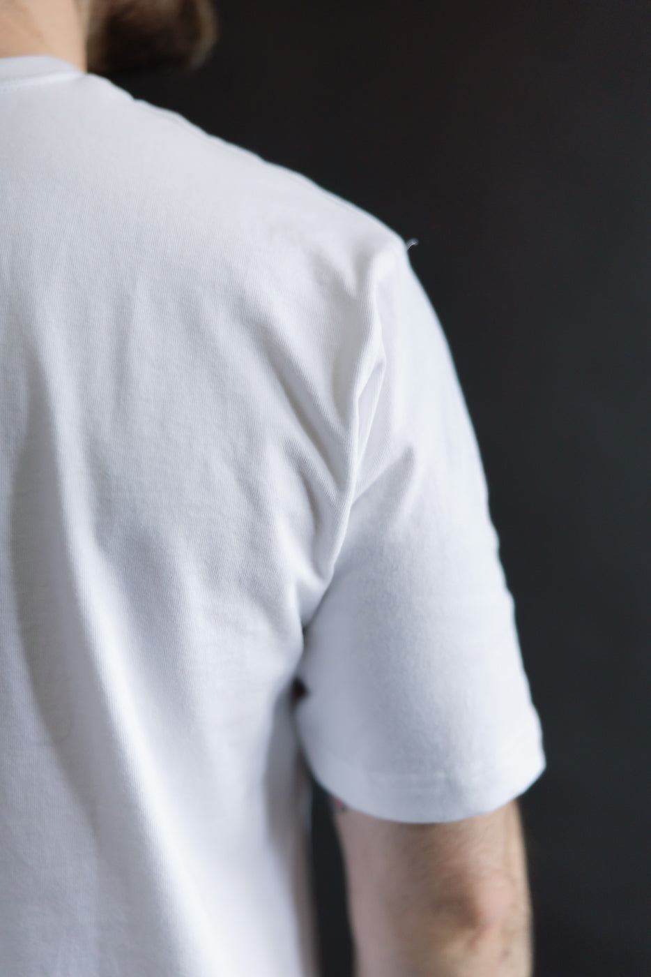 Close-up of back right shoulder and sleeve of white heavyweight boxy t-shirt on male model, 5'9