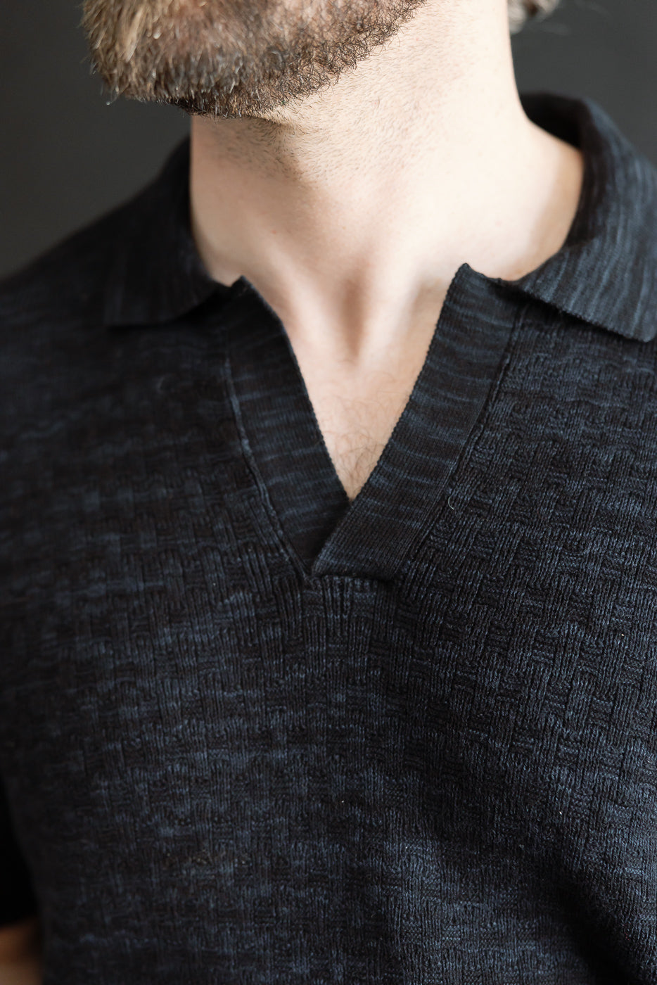 Close-up of male model wearing vintage black knit polo, front upper chest view showing textured boxweave fabric, open collar; model is 5'9