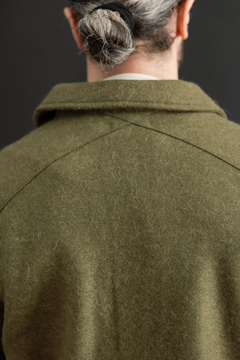 Close-up back view of a male model wearing an olive green wool coat showing the textured collar.