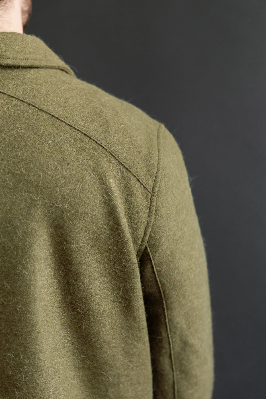 Close-up shot of the back and right shoulder of an olive green wool jacket showing fabric texture.