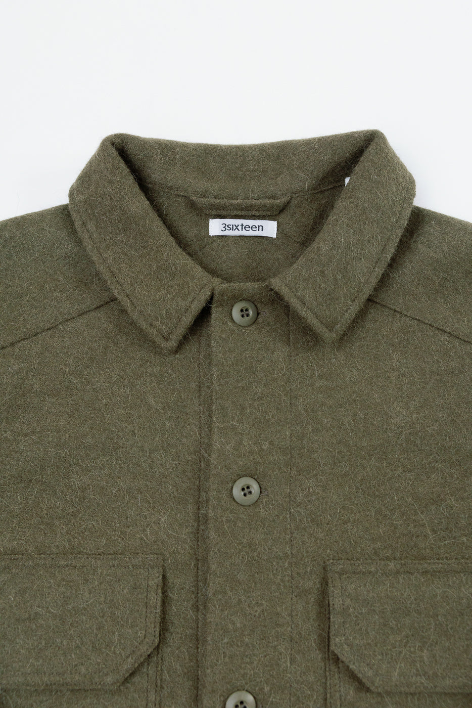 Close-up of the front collar and button details of an olive green wool shirt with a 3sixteen tag.