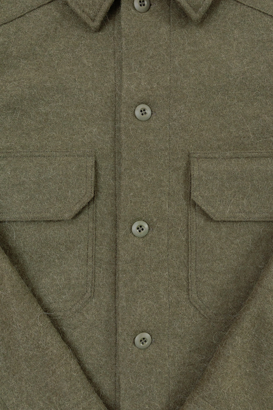 Close-up of the front of an olive wool shirt featuring buttons and chest pockets.