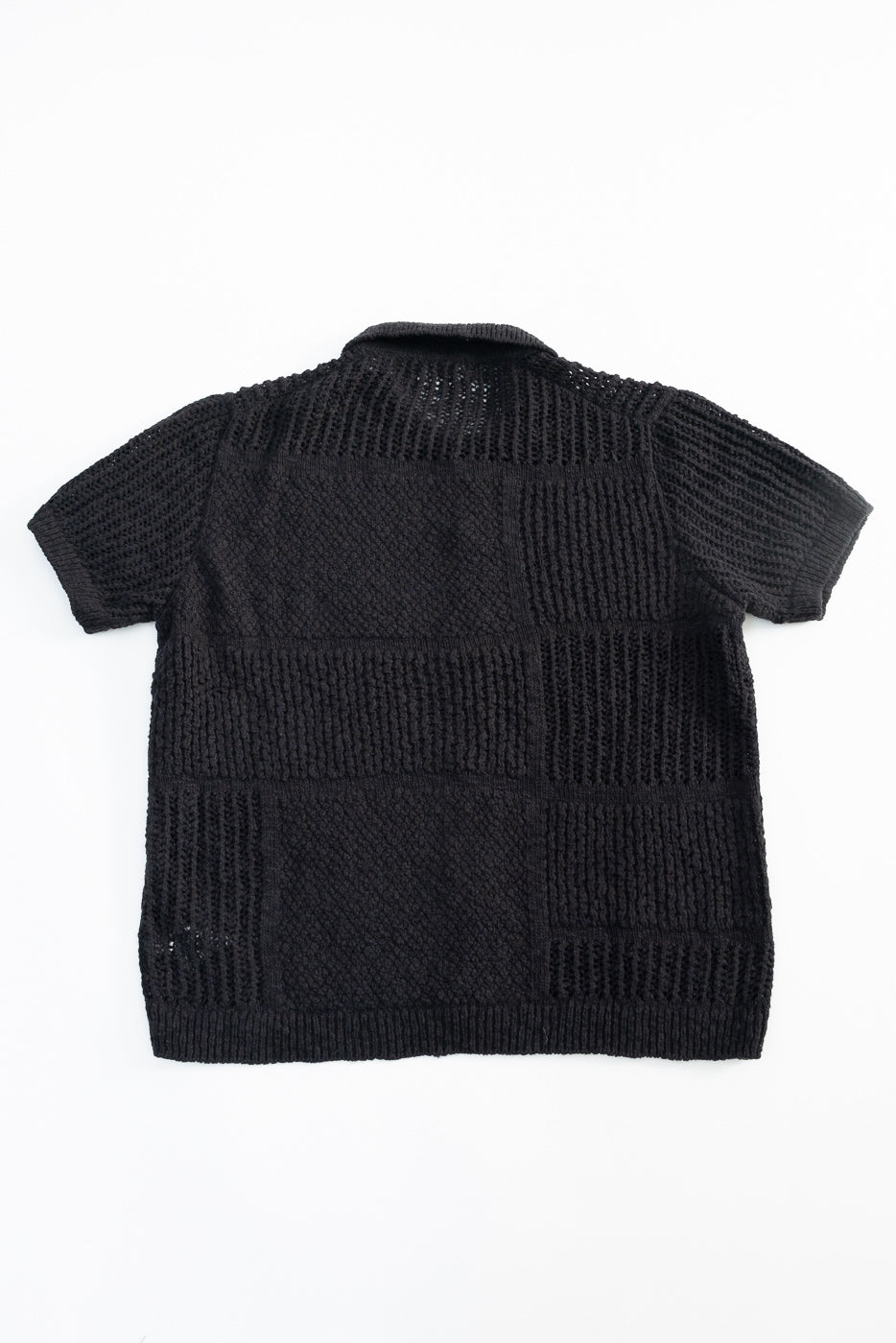 Flat lay of black short sleeve knit shirt, back view, showing textured patchwork knit pattern.