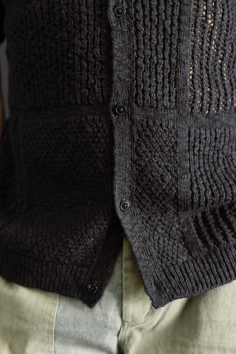 Close-up of a black knit shirt's textured front and black buttons on male model, waist view