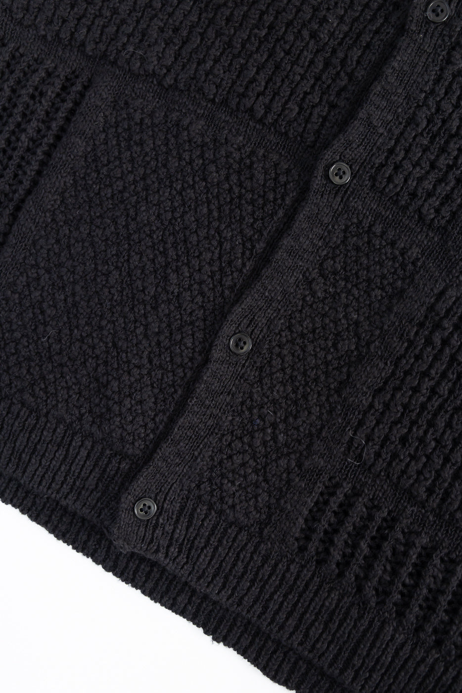 Close-up of black knit shirt front, showing textured fabric, ribbed hem, and buttons.