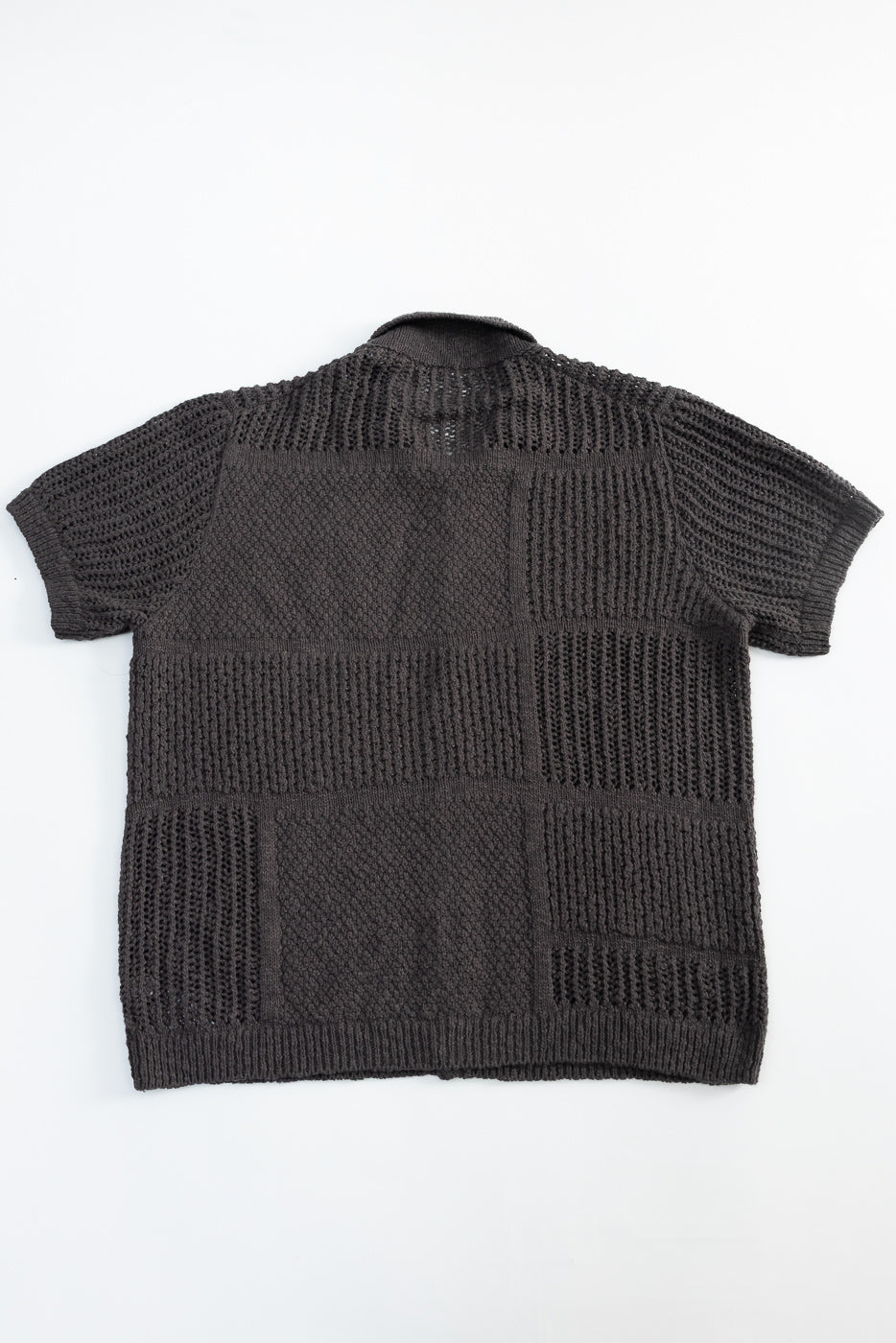Flat lay of short sleeve knit shirt, back view, showing textured patchwork pattern and ribbed hem.