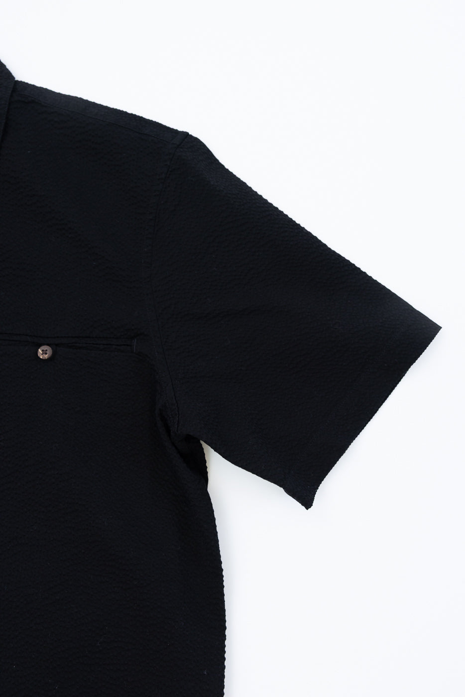 Close-up of the Short Sleeve Loop Shirt - Black Seersucker, showcasing the right sleeve, shoulder seam, and buttoned pocket detail, highlighting its textured cotton seersucker fabric and distinctive craftsmanship.