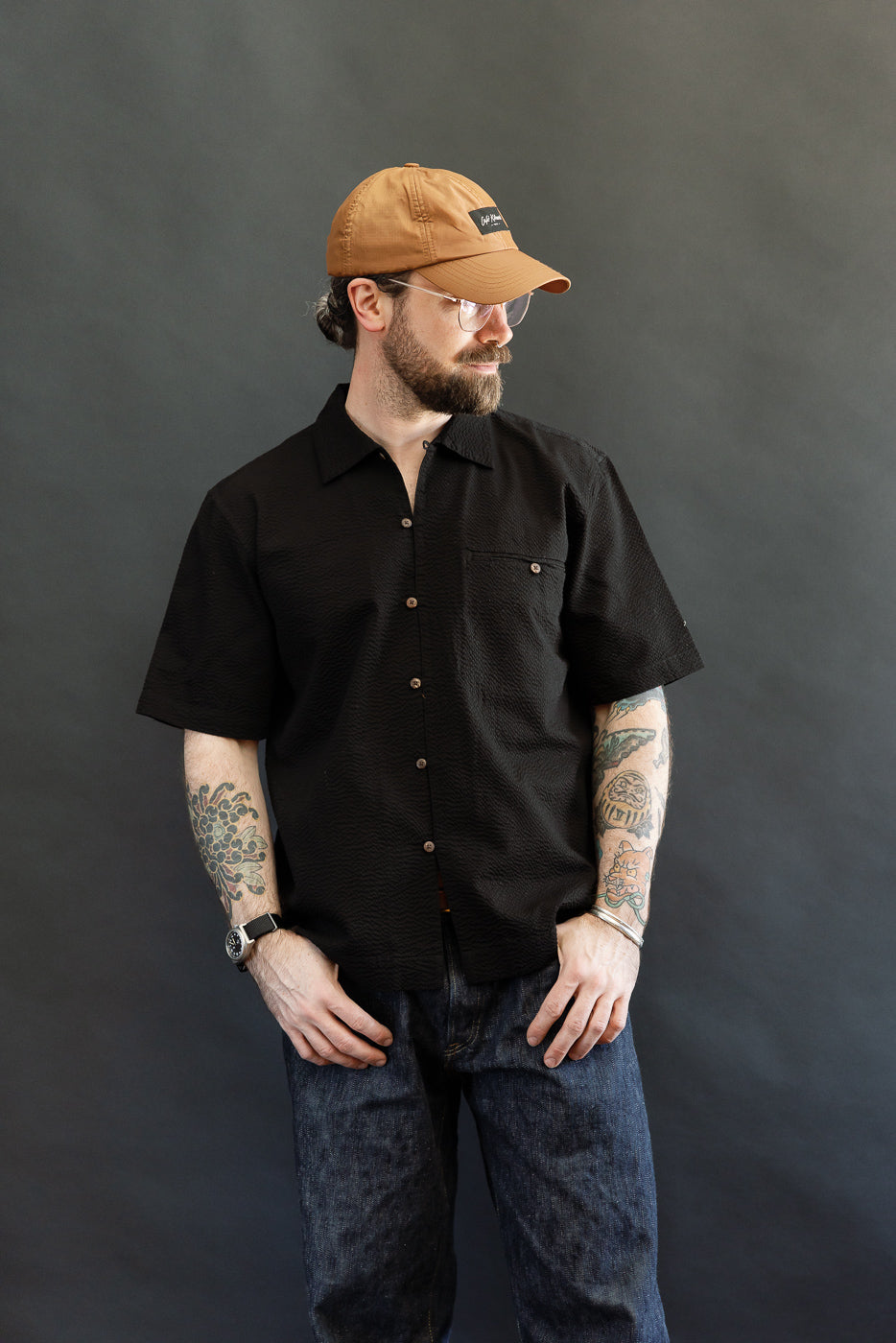 Bearded man models the Short Sleeve Loop Shirt - Black Seersucker, featuring a unique loop front placket, open collar, and single chest pocket, embodying Dant's premium menswear aesthetic.