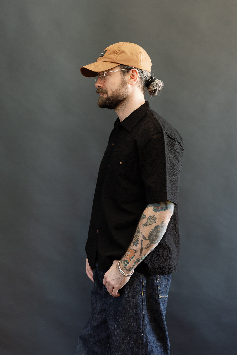 Side-profile of a man wearing the Short Sleeve Loop Shirt - Black Seersucker, showcasing the unique loop front placket and open collar against a medium-gray background.