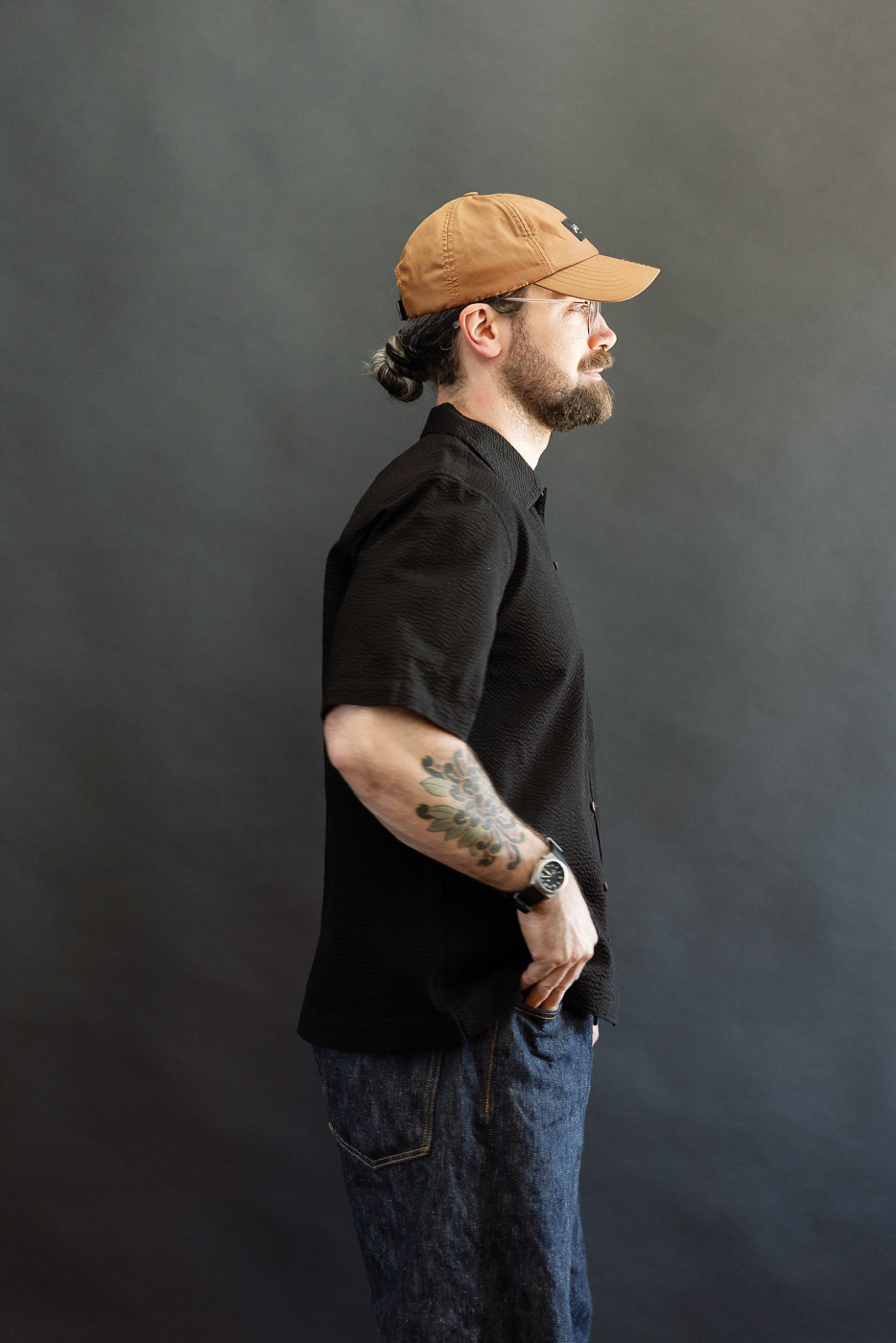 Bearded man in profile, wearing the Short Sleeve Loop Shirt - Black Seersucker, showcasing its loop front placket and open collar. The shirt exemplifies casual elegance with its distinctive seersucker texture.