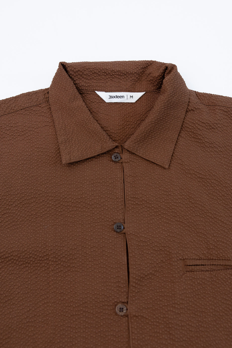 Short Sleeve Loop Shirt - Cinnamon Seersucker featuring a textured brown fabric, classic point collar, single chest welt pocket, and visible brown buttons, with a white label indicating 3sixteen | M inside the collar.