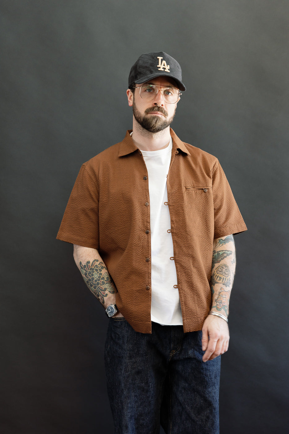 Model wearing the Short Sleeve Loop Shirt - Cinnamon Seersucker, showcasing its loop front placket and textured fabric, paired with dark blue denim jeans, exemplifying Dant's premium menswear style.