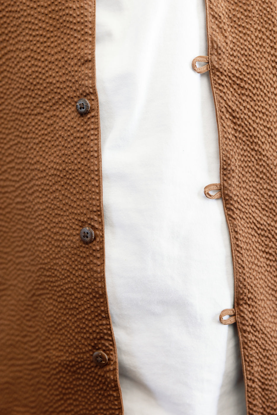 Short Sleeve Loop Shirt - Cinnamon Seersucker shown open over a white T-shirt, featuring textured brown fabric, loop front placket, and coconut shell buttons, highlighting its unique, utilitarian design.