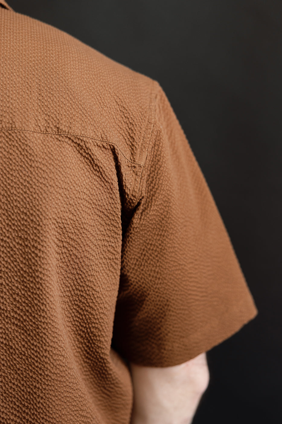 Close-up of the Short Sleeve Loop Shirt - Cinnamon Seersucker, highlighting the textured fabric and unique loop placket, embodying a blend of utilitarian design and warm-weather practicality.