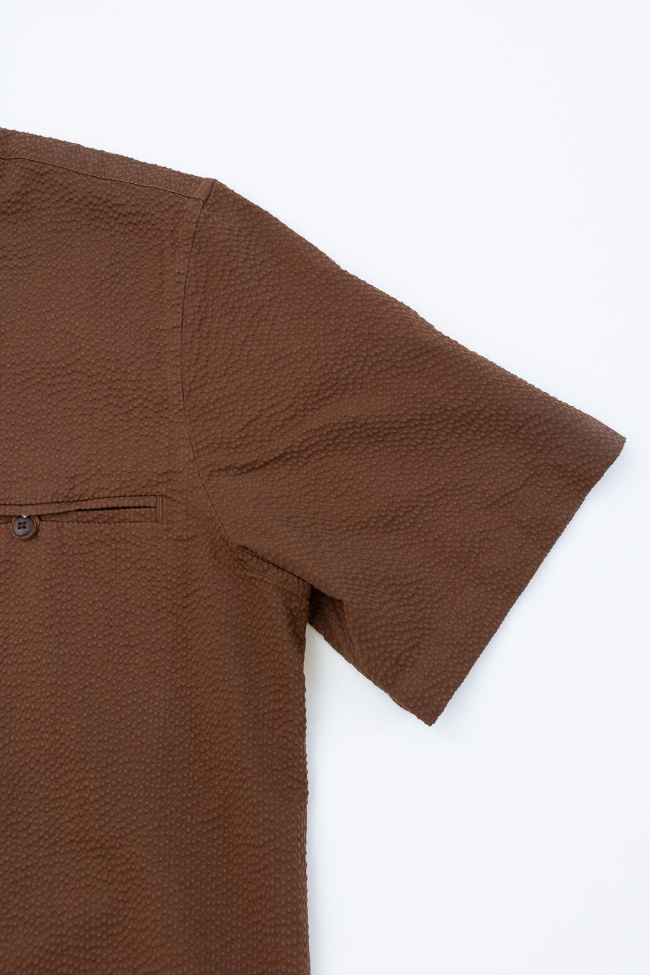 Short Sleeve Loop Shirt - Cinnamon Seersucker features a textured brown design with a welt pocket and coconut shell button. Made from crisp 100% cotton seersucker, it's laid flat highlighting its loop placket detail.