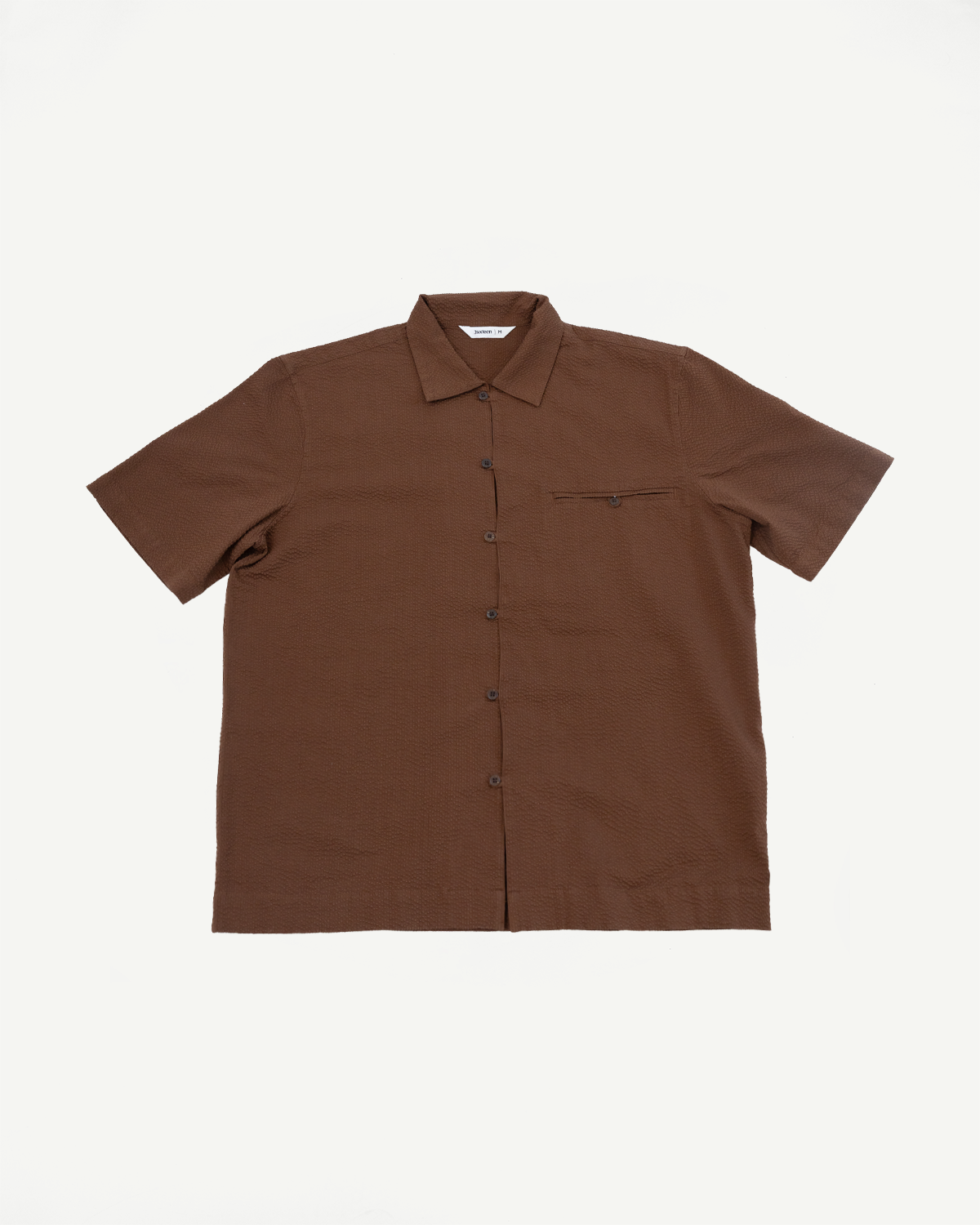 Short Sleeve Loop Shirt - Cinnamon Seersucker: A brown, short-sleeved, collared button-up shirt with fabric loops instead of buttonholes, a single left chest pocket, and coconut shell buttons, laid flat on a white background.