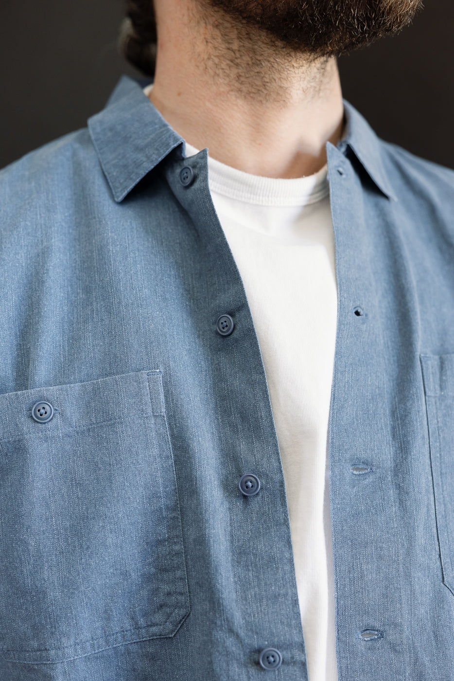 Close-up of the 3sixteen Short Sleeve Work Shirt in blue pigment dye, showcasing dual cut-corner chest pockets and Corozo buttons over a white T-shirt, highlighting its vintage-washed character.