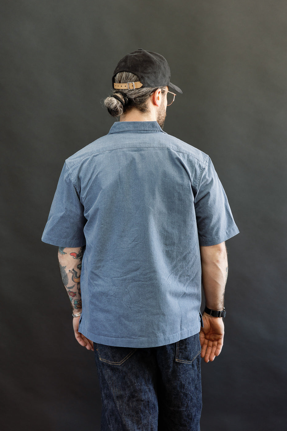 Adult male model wearing the 3sixteen Short Sleeve Work Shirt in Blue Pigment Dye, showcasing a modern workwear style with dual cut-corner chest pockets and Corozo buttons, paired with dark jeans.
