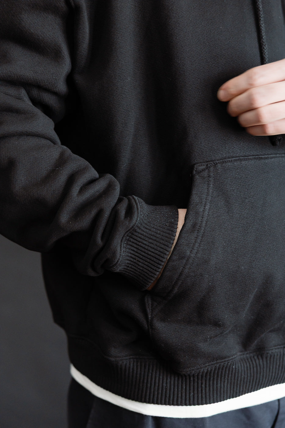 Close-up of 3sixteen Ultraweight black pullover hoodie front pocket, worn by male model, athletic build, showcasing ribbed cuffs and hem.