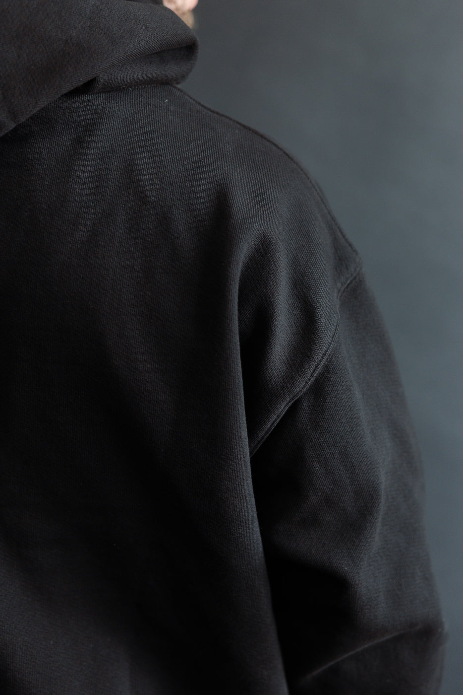 Close-up back view of black ultraweight pullover hoodie fabric on male model, Dant shop