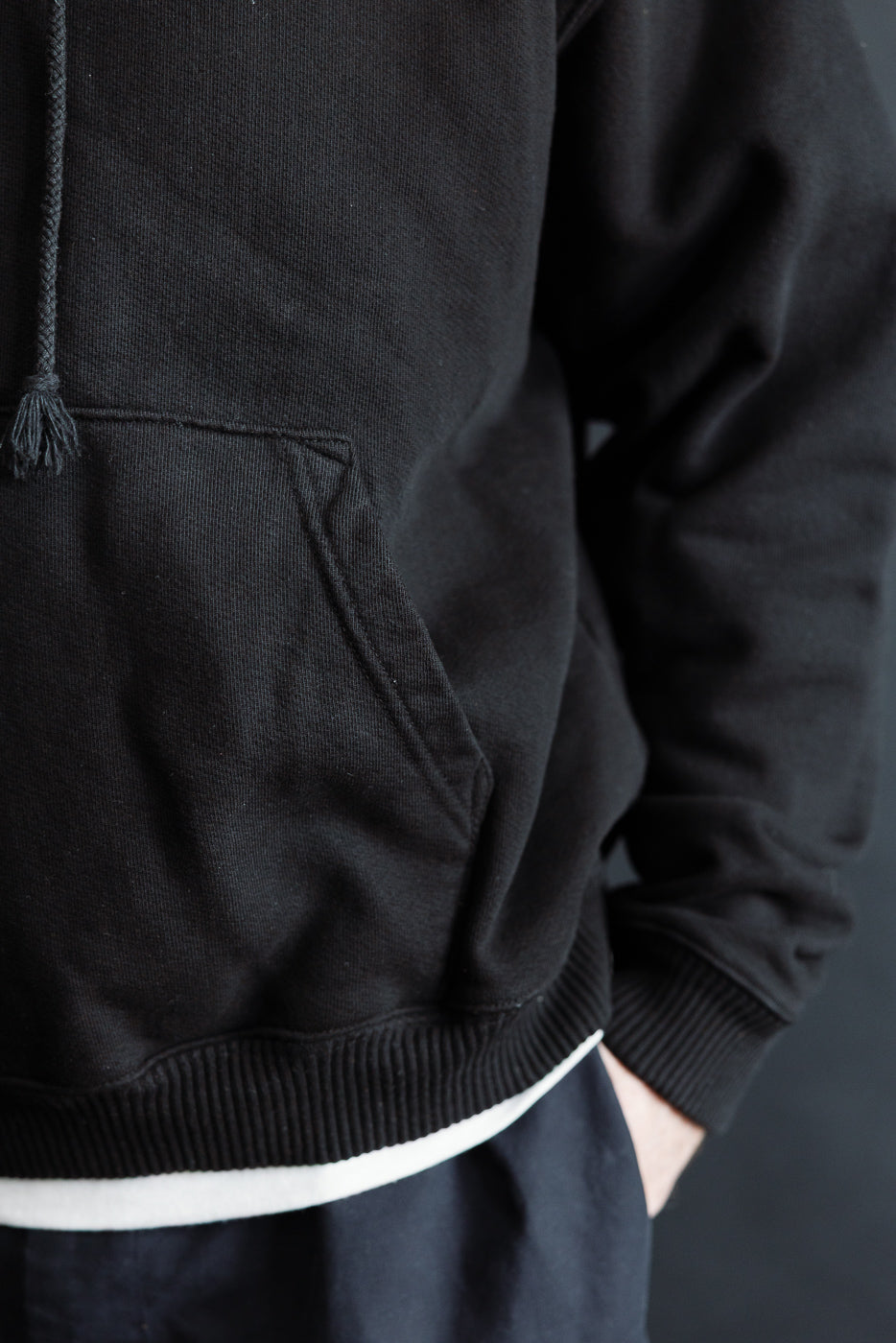 Close-up front view of black 3sixteen ultraweight pullover hoodie kangaroo pocket, on male model 5'9