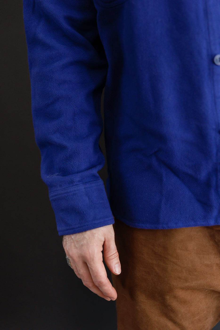 Close-up side view of a male model's arm and blue corduroy shirt sleeve and cuff.