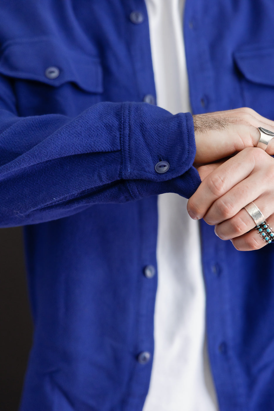 Close-up of the front cuff and sleeve of a blue button-down shirt on a male model.