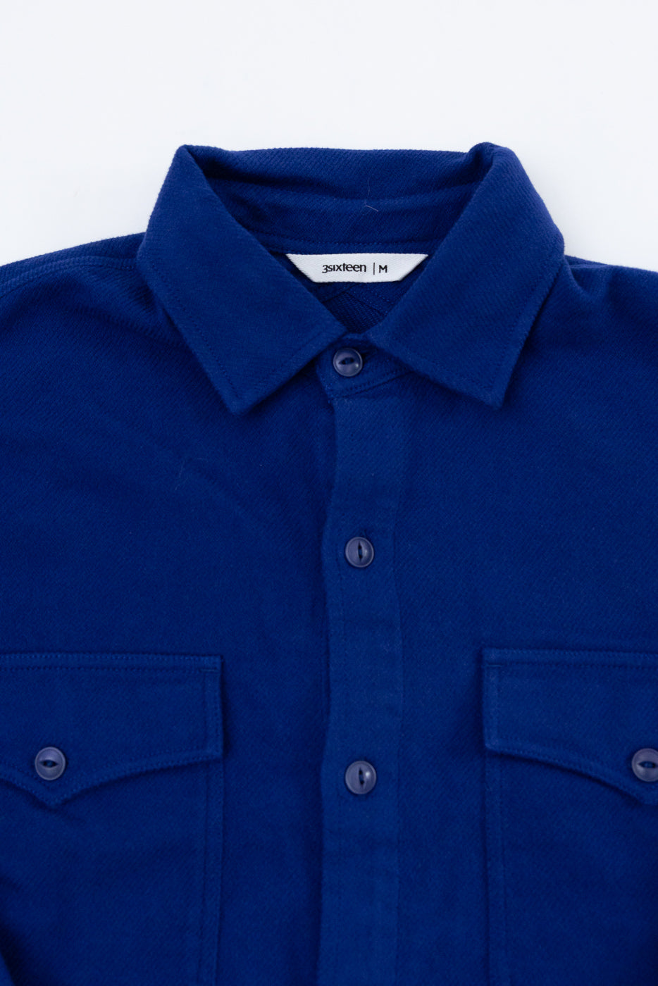 Close-up front view of a blue button-down shirt showing collar, texture, and chest pockets.
