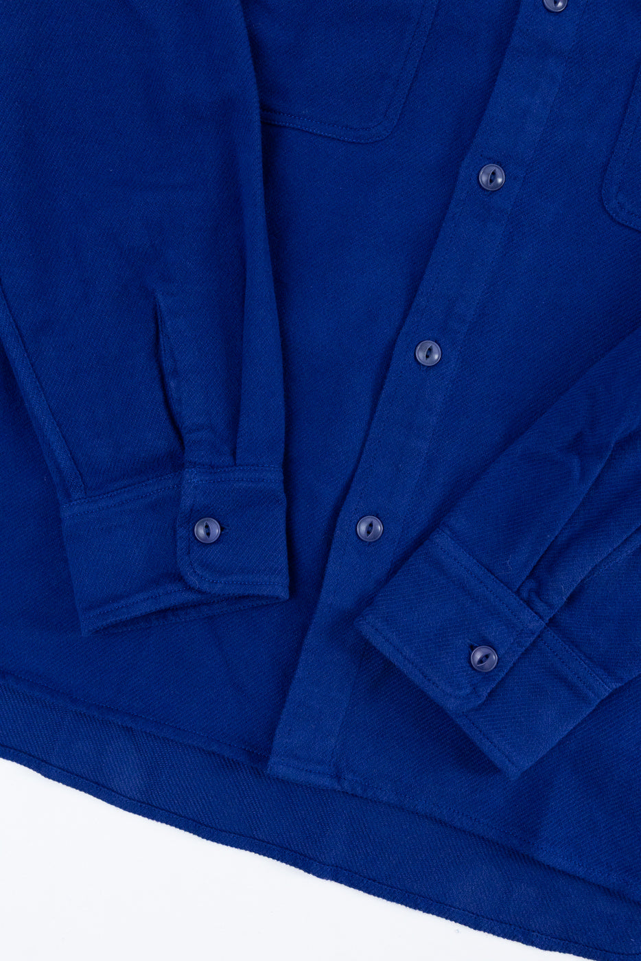 Close-up of the front of a blue shirt showing buttons, fabric texture, and cuff details.