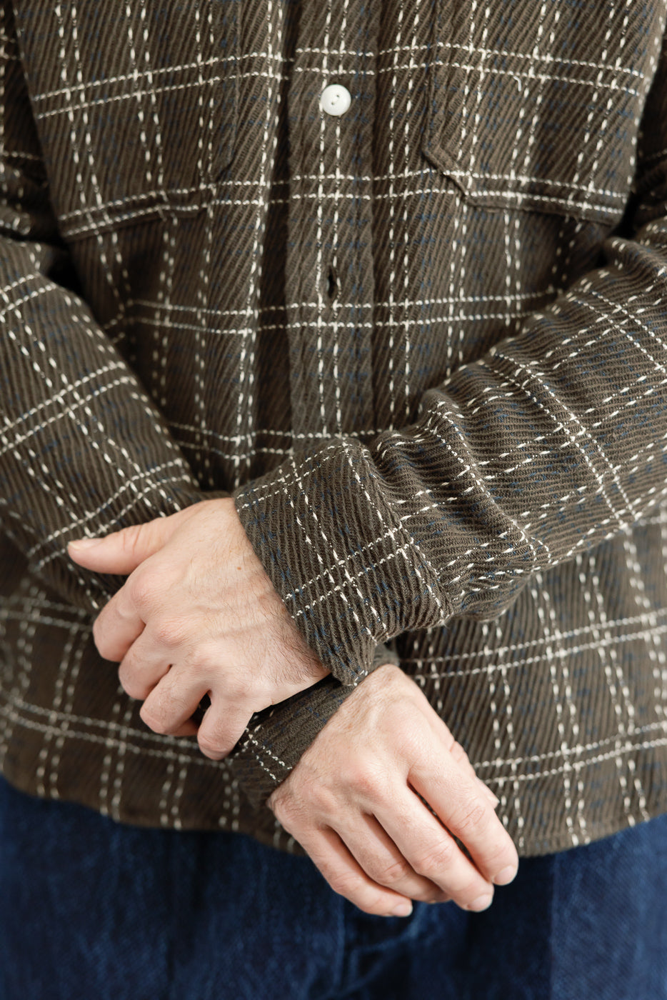 Close-up front view of a male model's arms in a brown plaid flannel shirt showing sleeve cuffs.