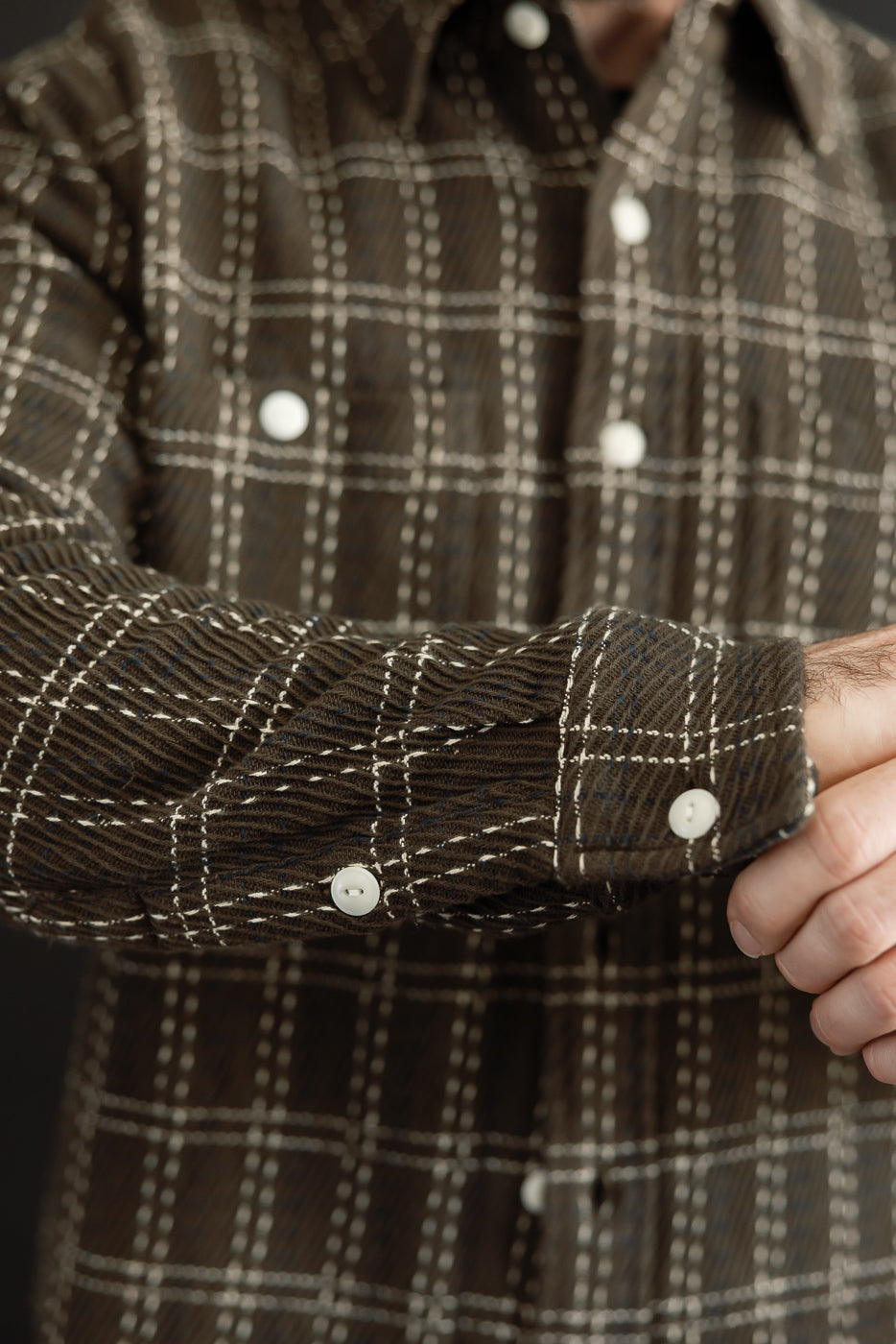 Close-up of the cuff and sleeve of a brown plaid flannel shirt showing white buttons and texture.