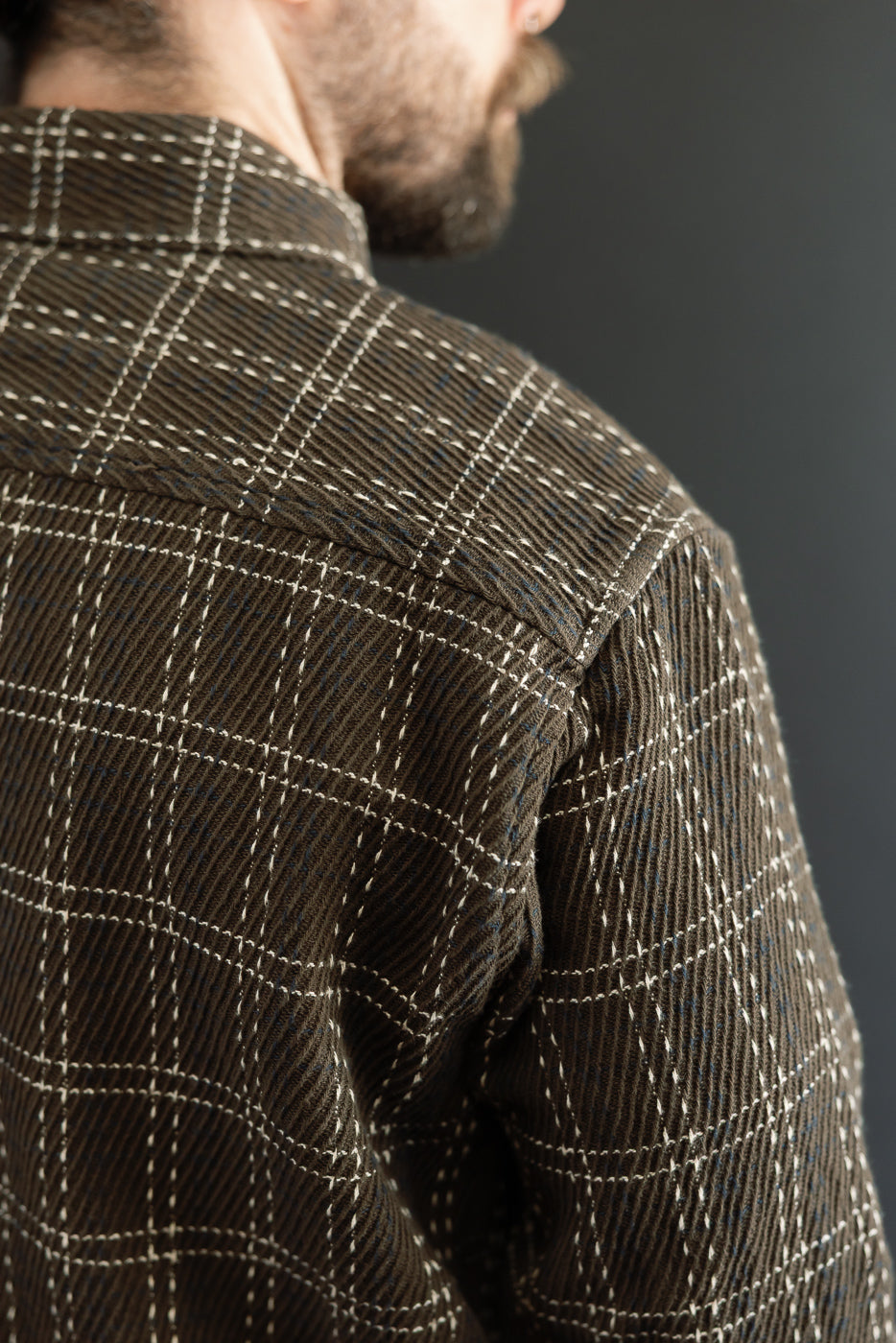 Close-up back view of a male model's brown plaid textured shirt showing shoulder and sleeve detail.