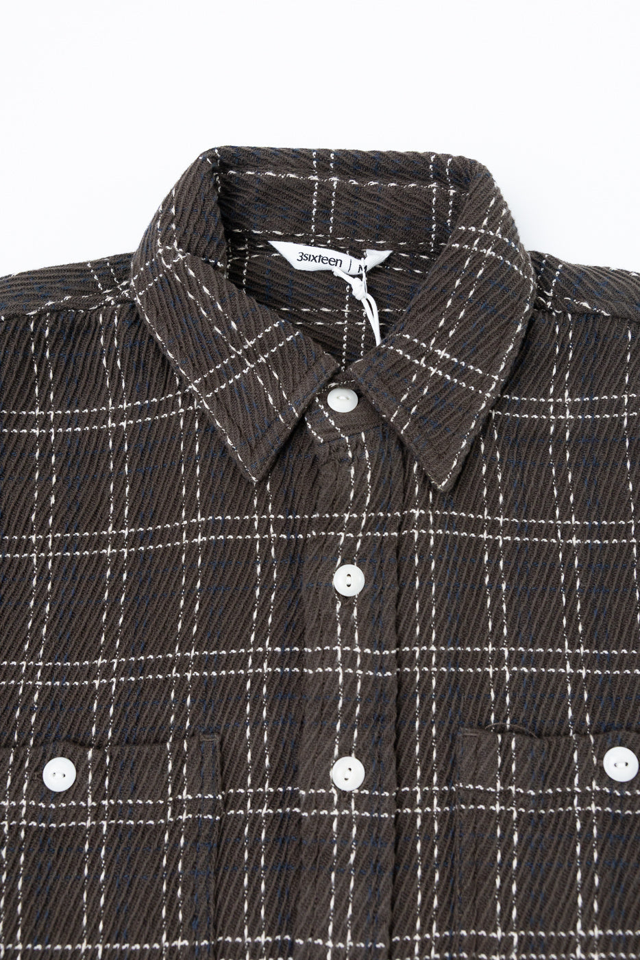 Close-up front view of a brown plaid flannel shirt showing fabric texture and white buttons.