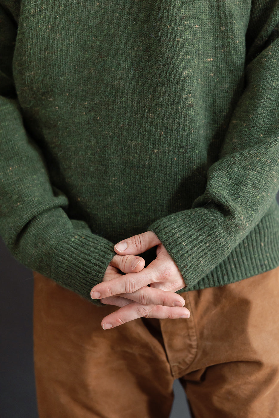 Close-up front view of a male model wearing a textured green knit sweater and brown trousers.