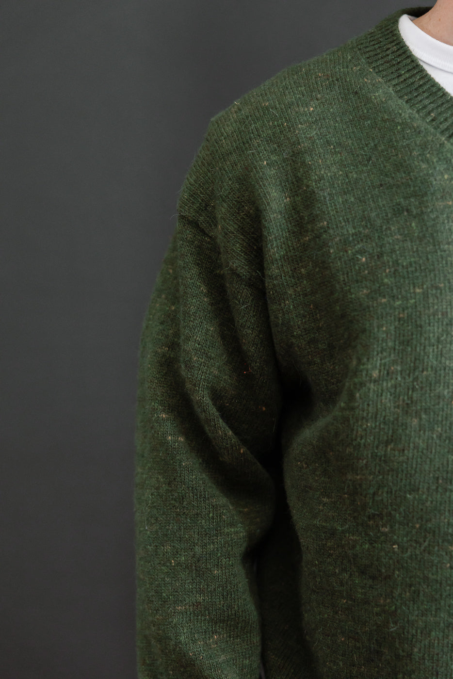 Close-up of the side view and sleeve texture of a green knit sweater worn by a male model.