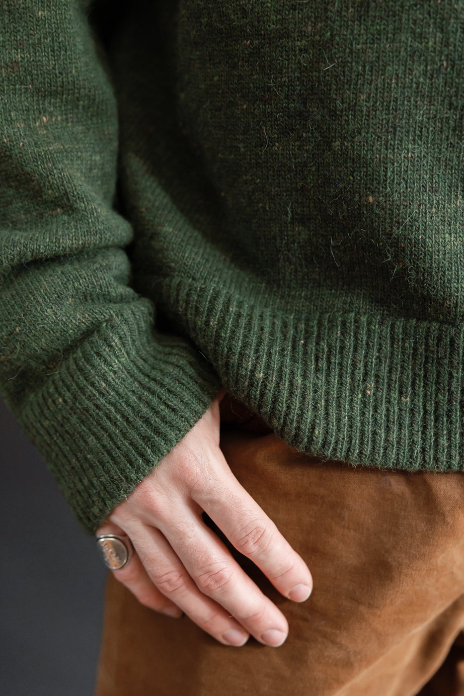 Close-up of the ribbed cuff and textured knit fabric of a green sweater on a male model.