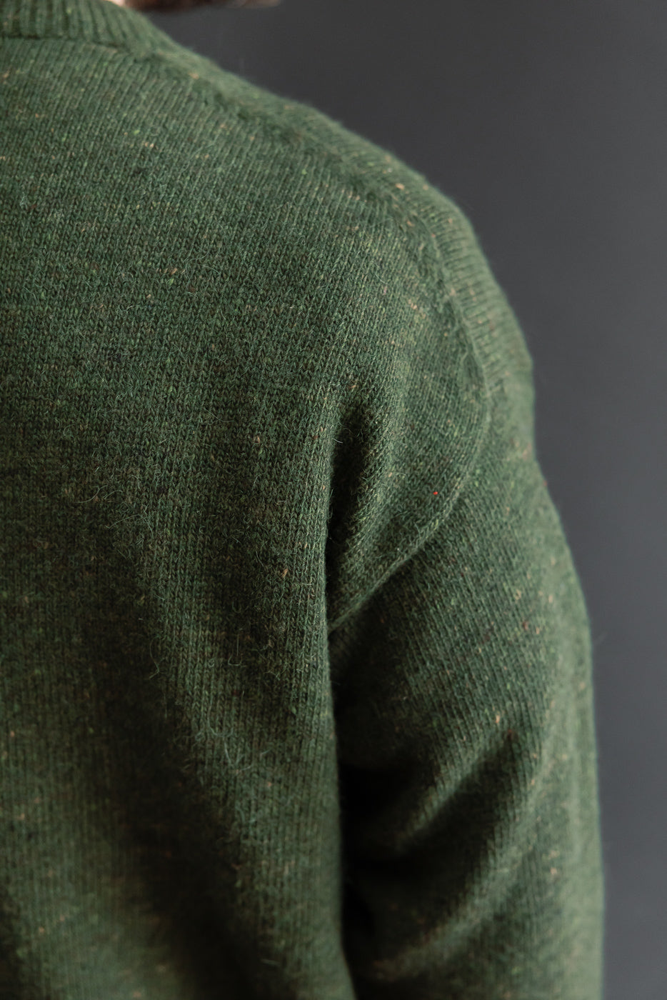 Close-up of the shoulder and sleeve texture of a green knit sweater.