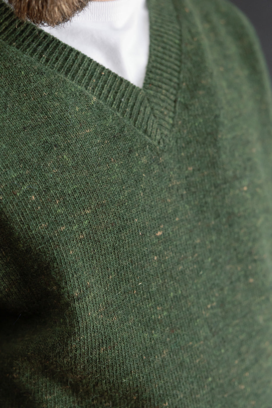 Close-up of the V-neck collar and textured wool fabric of a green sweater.