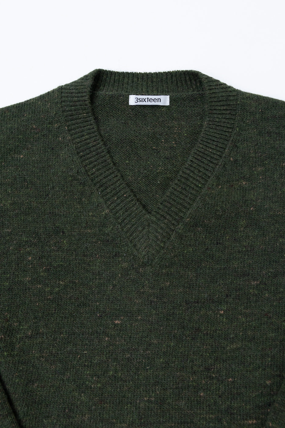 Close-up of the front V-neck collar and white 3sixteen neck tag on a dark green knit sweater.
