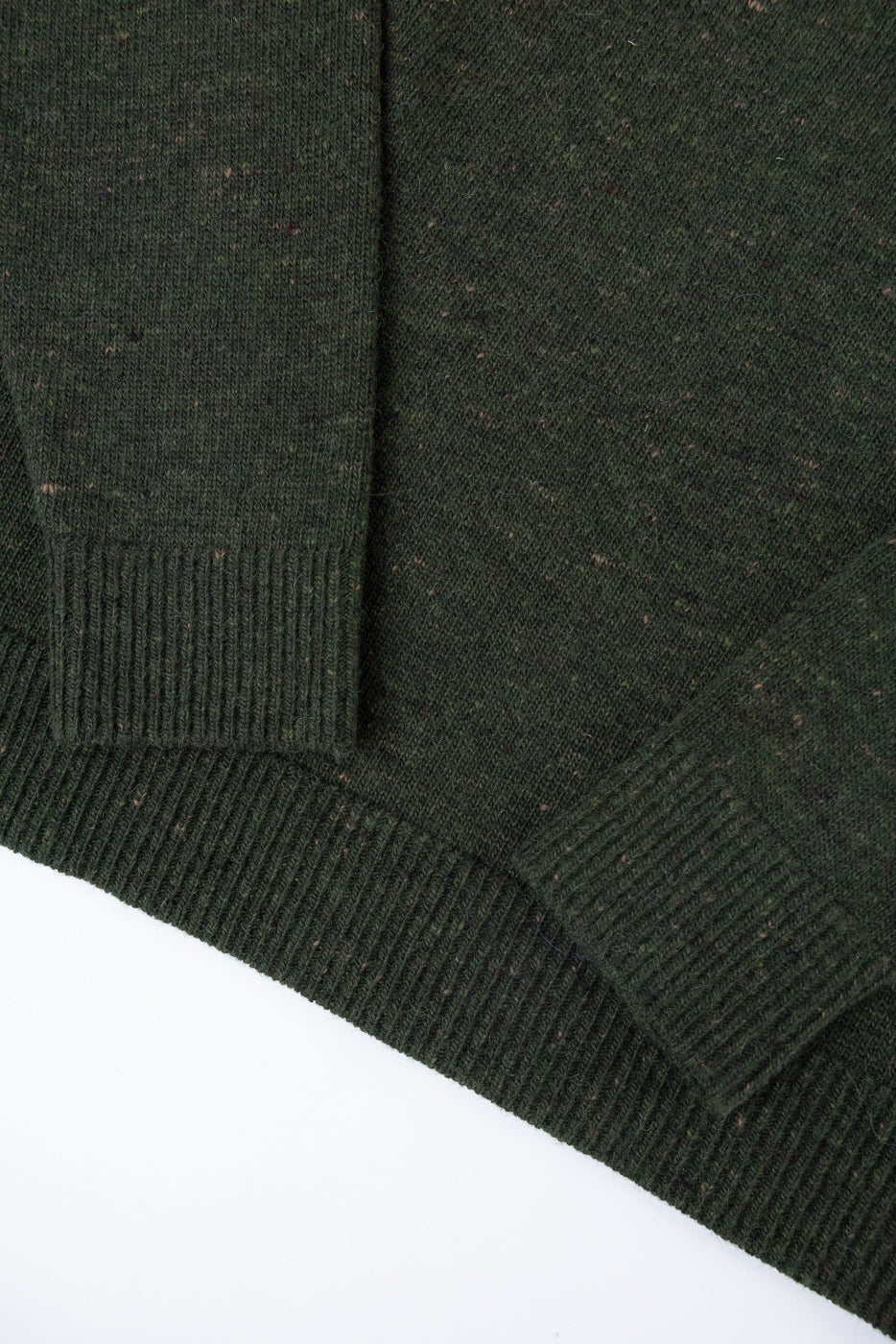 Close-up of the ribbed cuffs and hem of a dark green textured knit sweater.